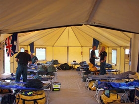 Interior of a large tent with rows of simple camp beds set up
