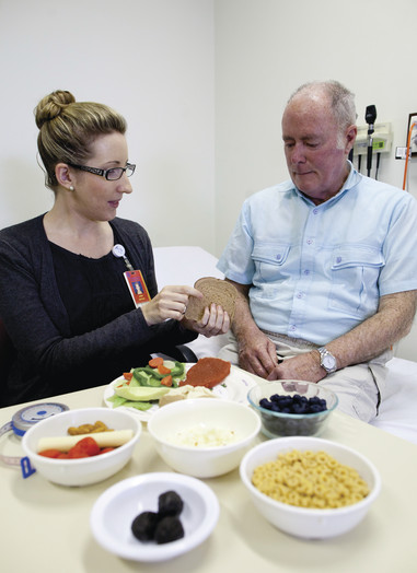 Female health professional showing examples of healthy foods to an older male patient.