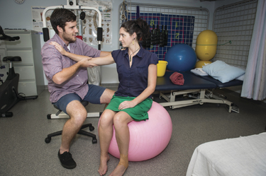 Patient sitting on fit ball while health care professional is holding her arm